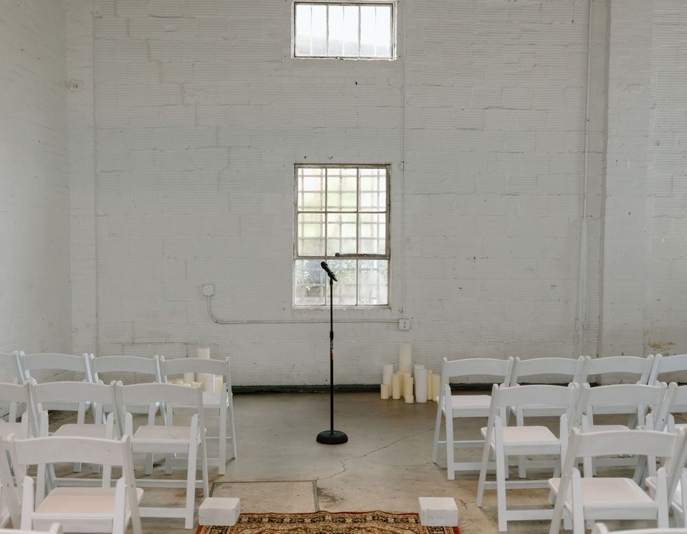 A minimalist white wedding ceremony space with rows of chairs and natural light from windows.