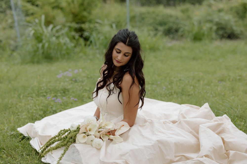 A bride in a flowing white dress poses in a grassy meadow with a bouquet.