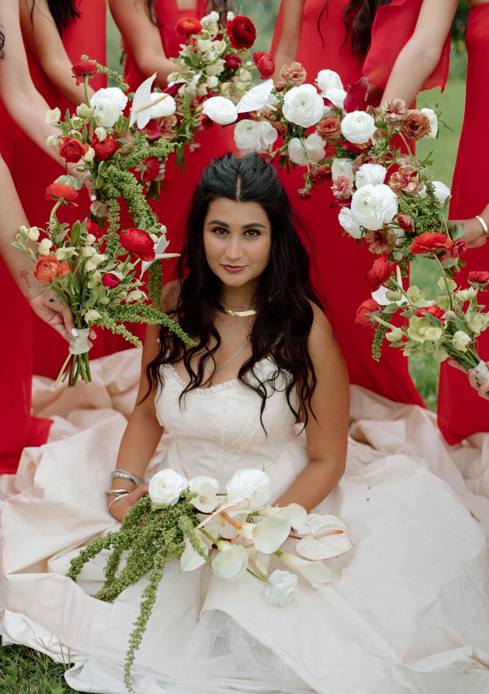 A bride in white surrounded by bridesmaids in red holding floral bouquets.