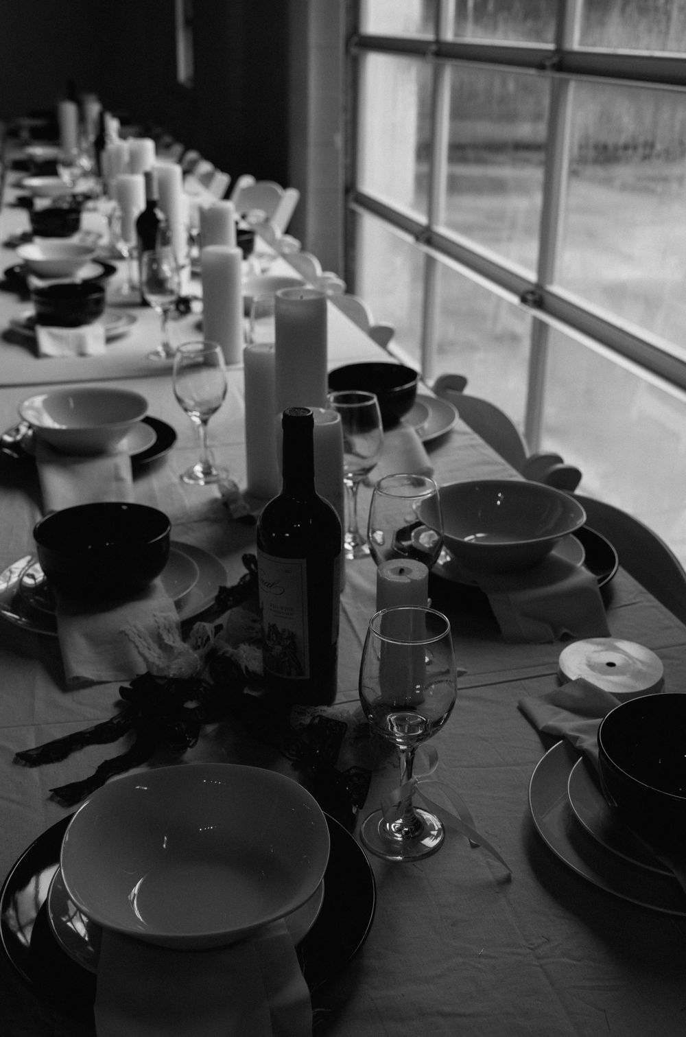 Elegant table setting with wine glasses, plates and candles arranged by a window in black and white.