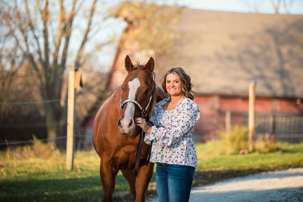 A brown horse and rider stand together in a rustic outdoor setting during a photo session.