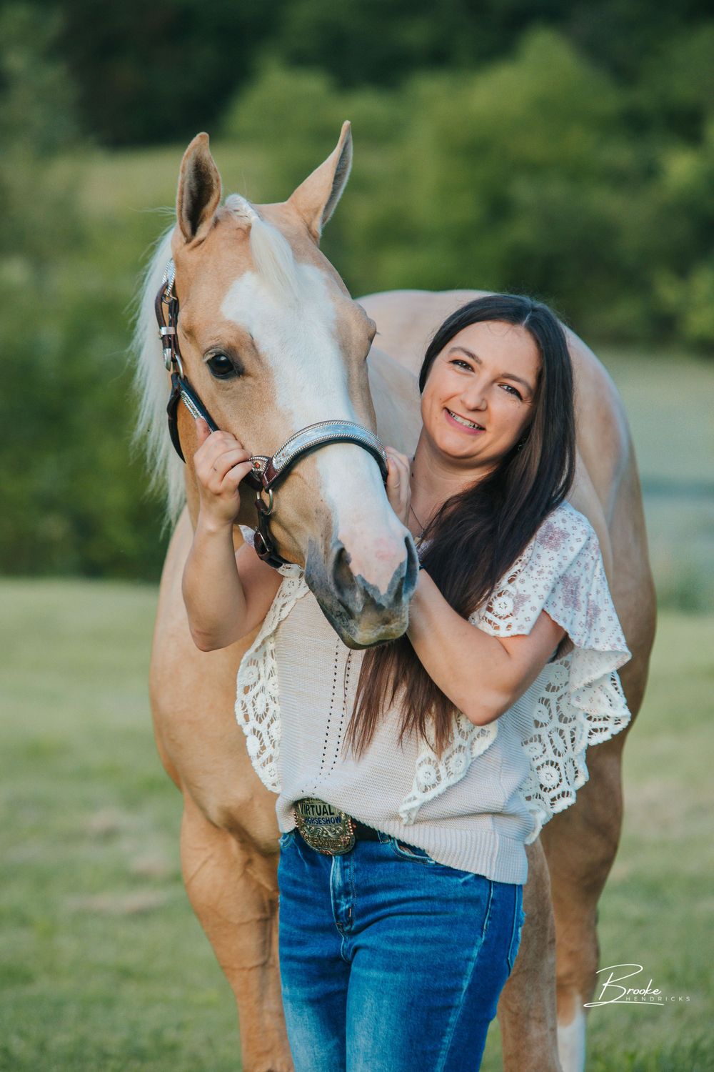 A palomino horse and someone in a white lace top share an affectionate moment outdoors.