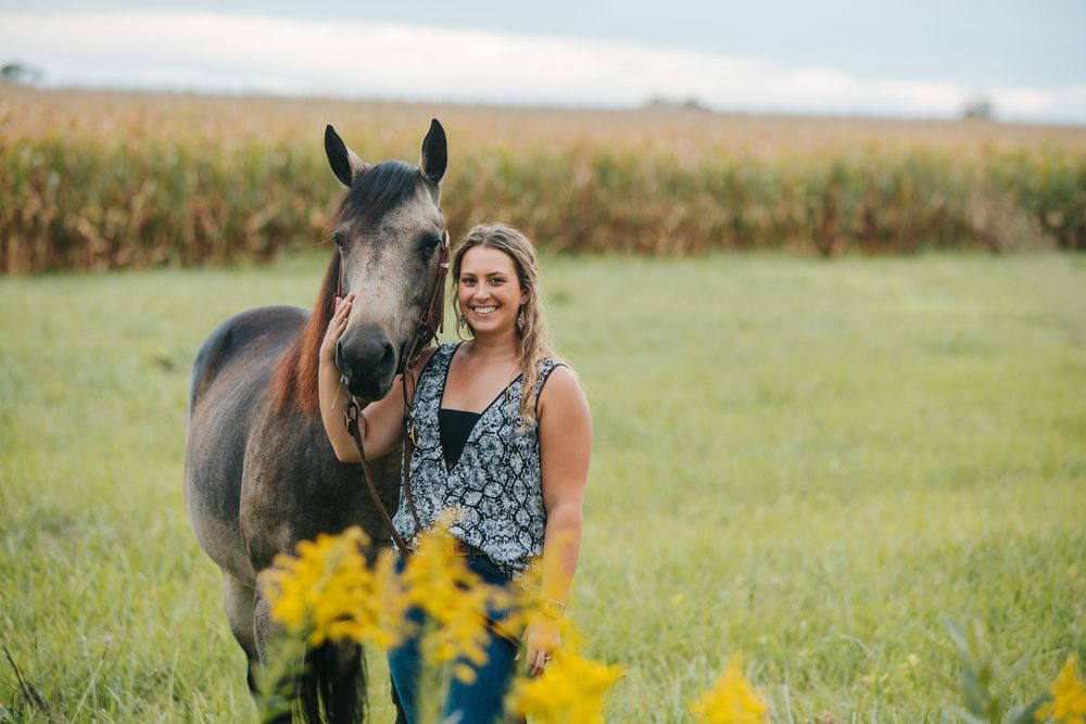 Horse and rider in a sunny field with yellow wildflowers blooming.