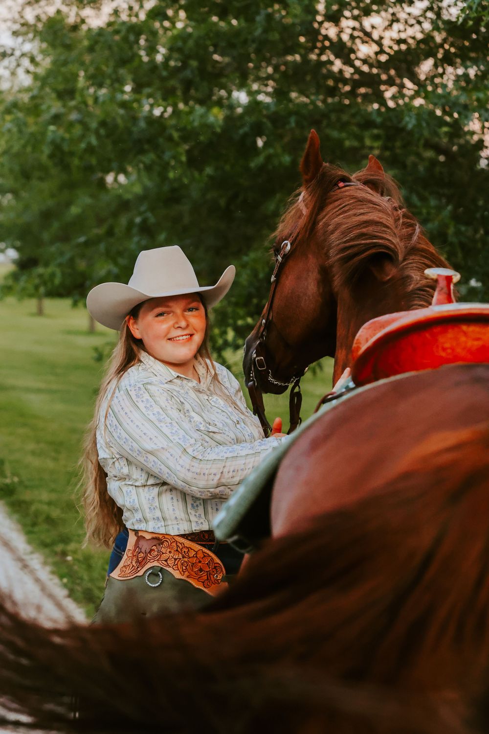 Person in western attire and cowboy hat with brown horse at sunset.