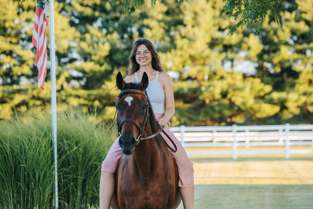 Someone rides a dark brown horse past an American flag and white fencing.