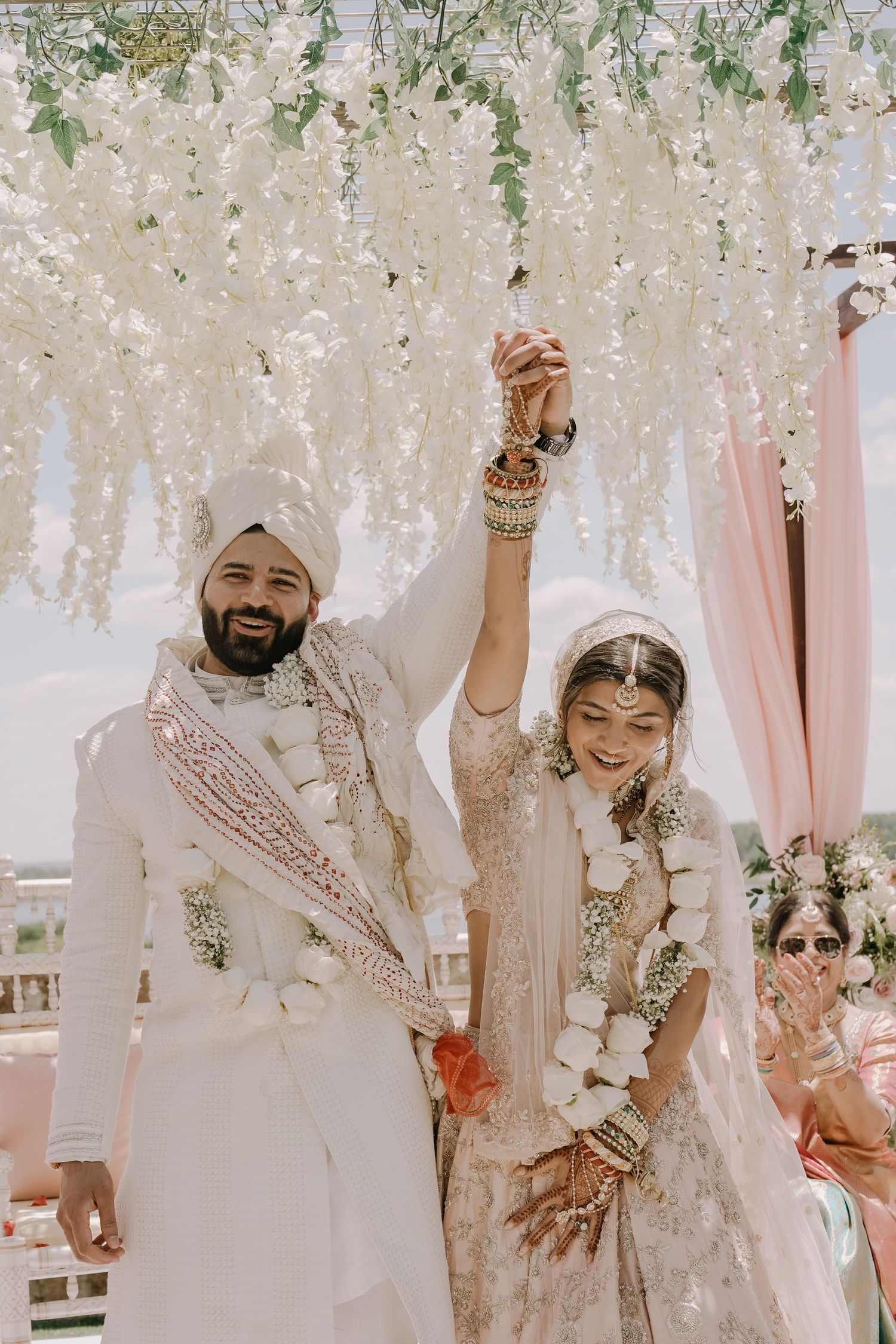 Traditional Indian wedding ceremony with couple holding hands under white floral mandap decorations.