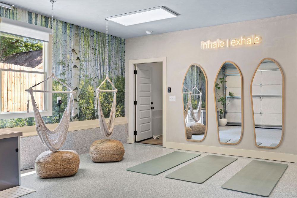Serene yoga studio with hanging rope chairs, arched mirrors, green mats, and an Inhale Exhale neon sign on the wall.