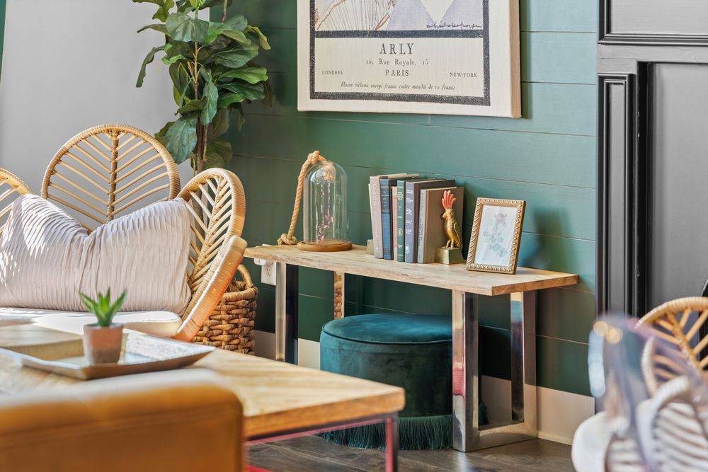 Bohemian living room with rattan chairs, teal velvet ottoman, gold accents, and green shiplap walls with framed art.