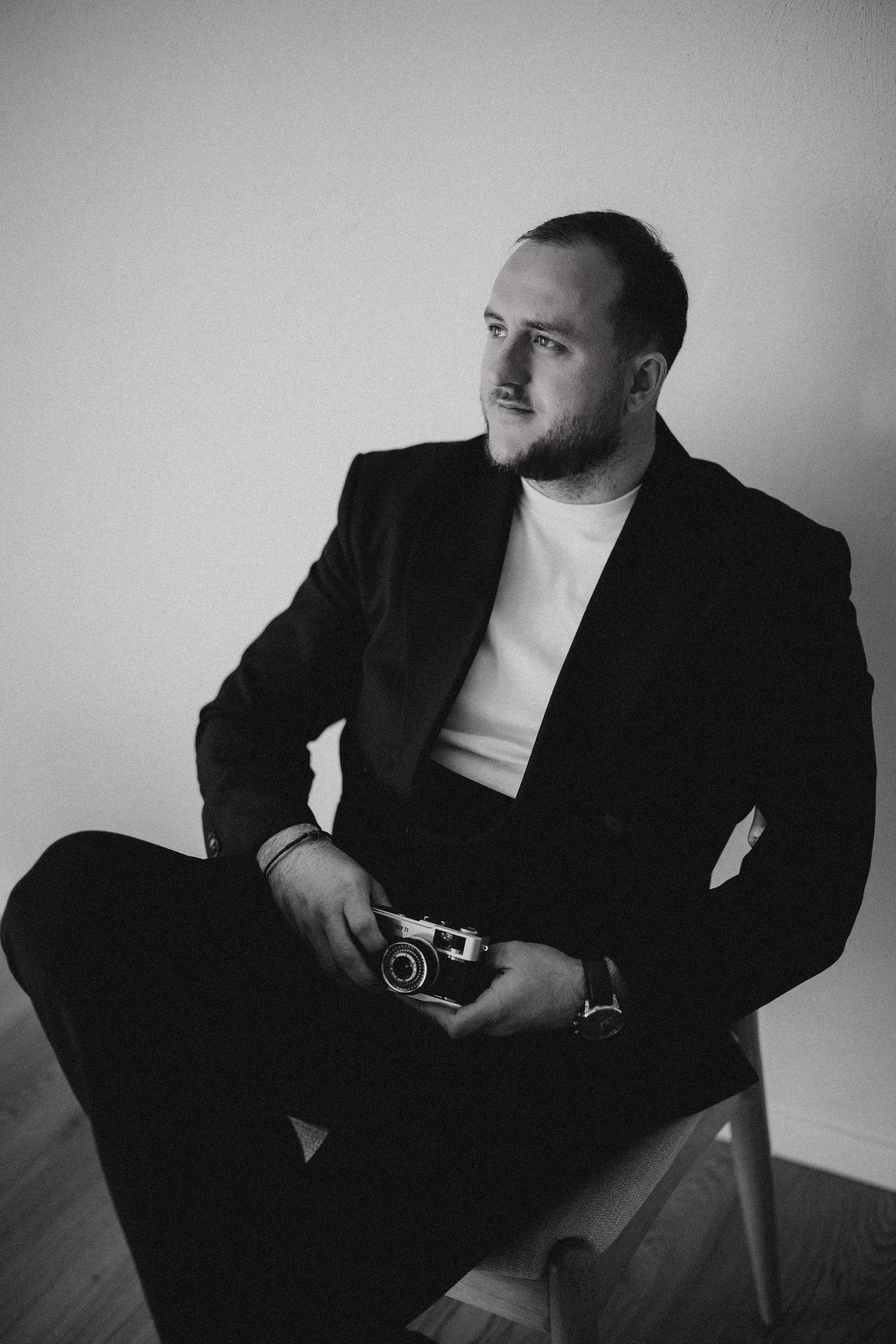 Portrait of person in dark jacket holding camera against brown backdrop.