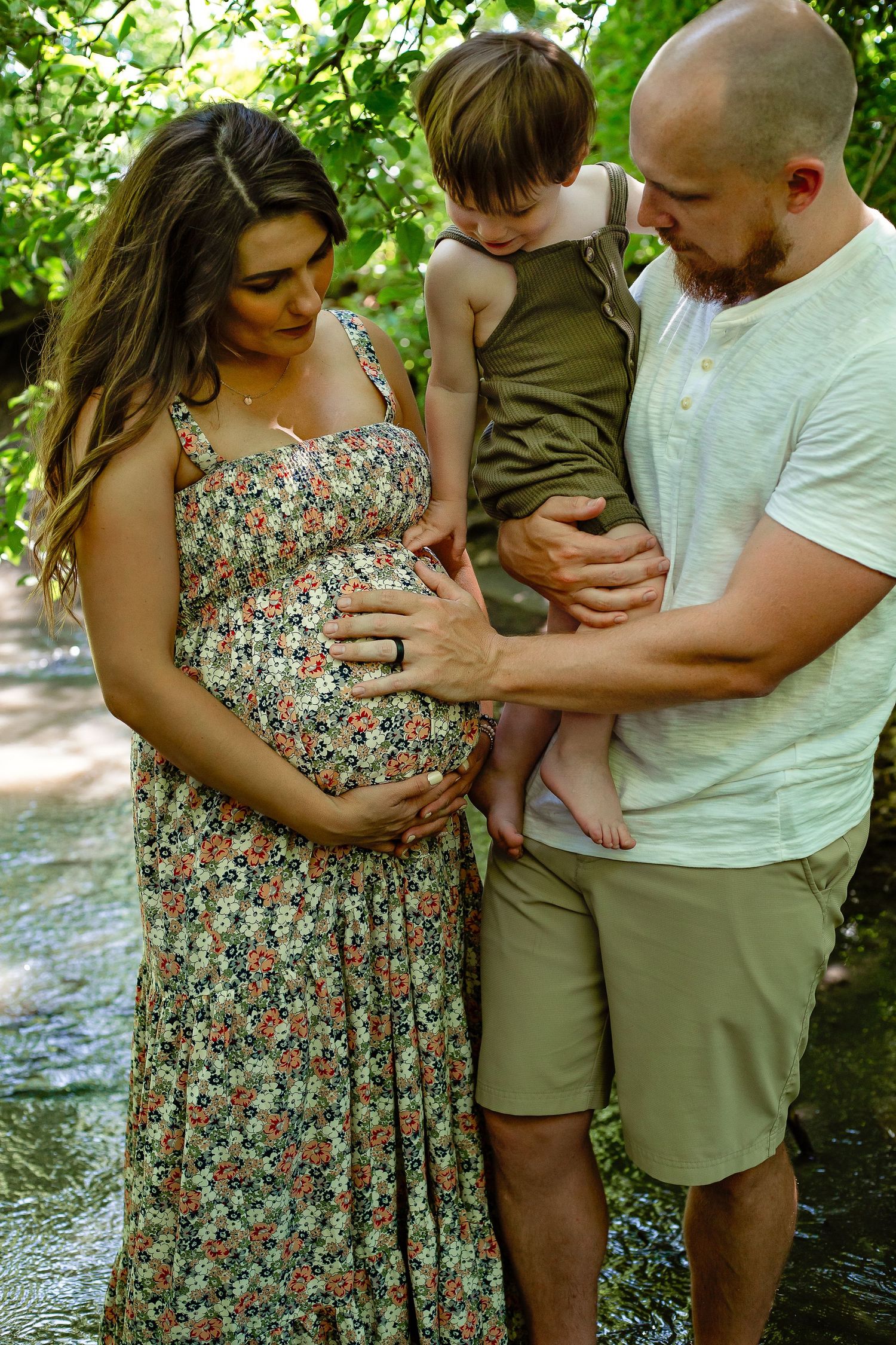 An intimate outdoor maternity photo with a floral dress and gentle touches in a natural setting.