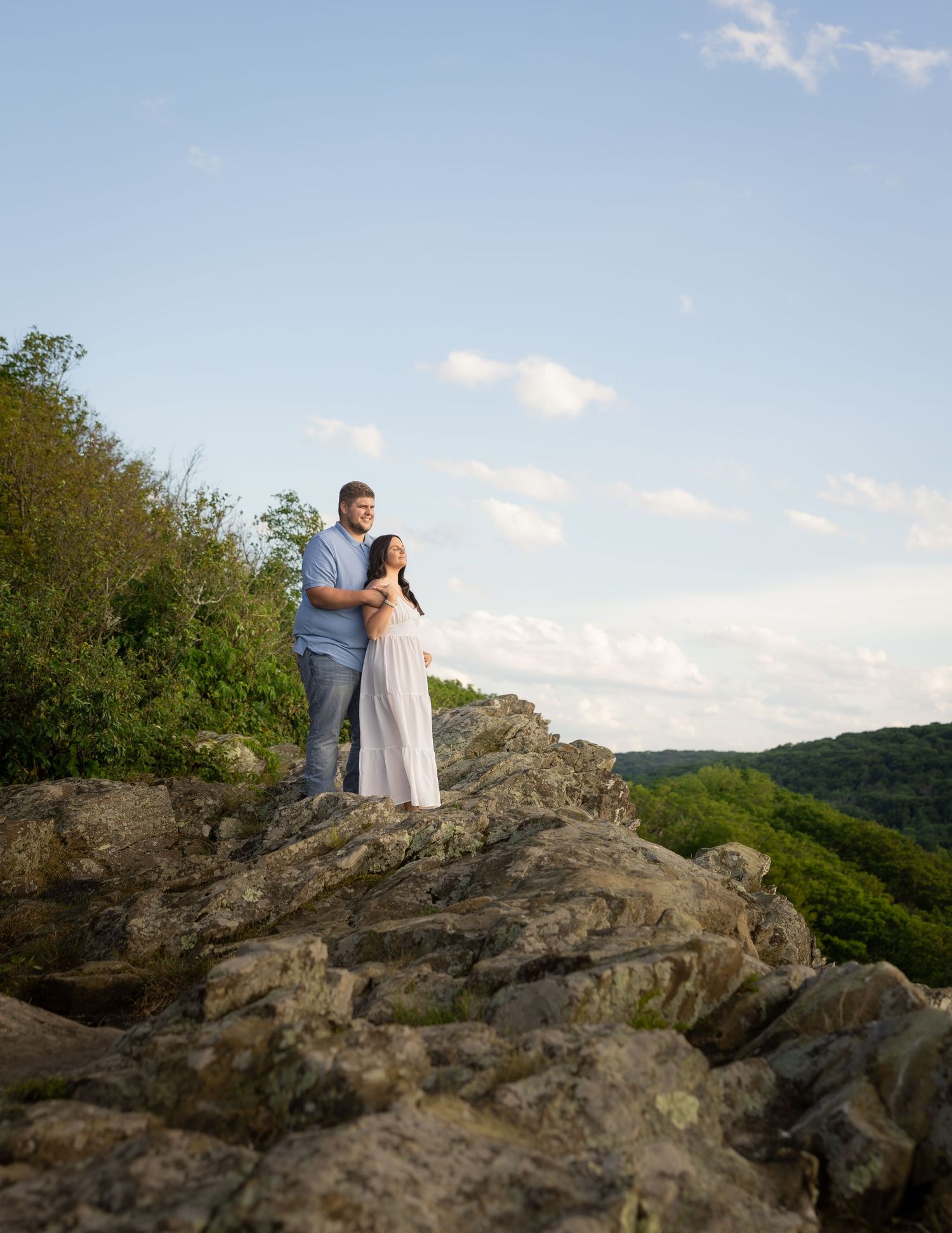 Rocky cliff edge overlooks vast forest valley under clear blue sky.