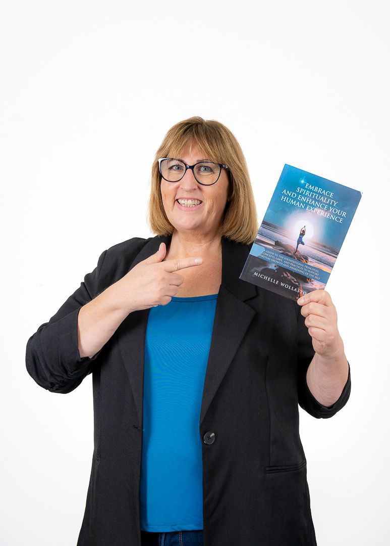 Woman in blue shirt and blazer smiling while pointing at and holding a self-help book.