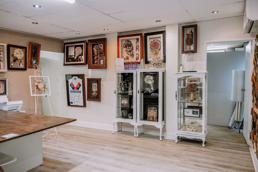 A gallery wall displays framed artwork and memorabilia in a bright white room with light wood flooring.