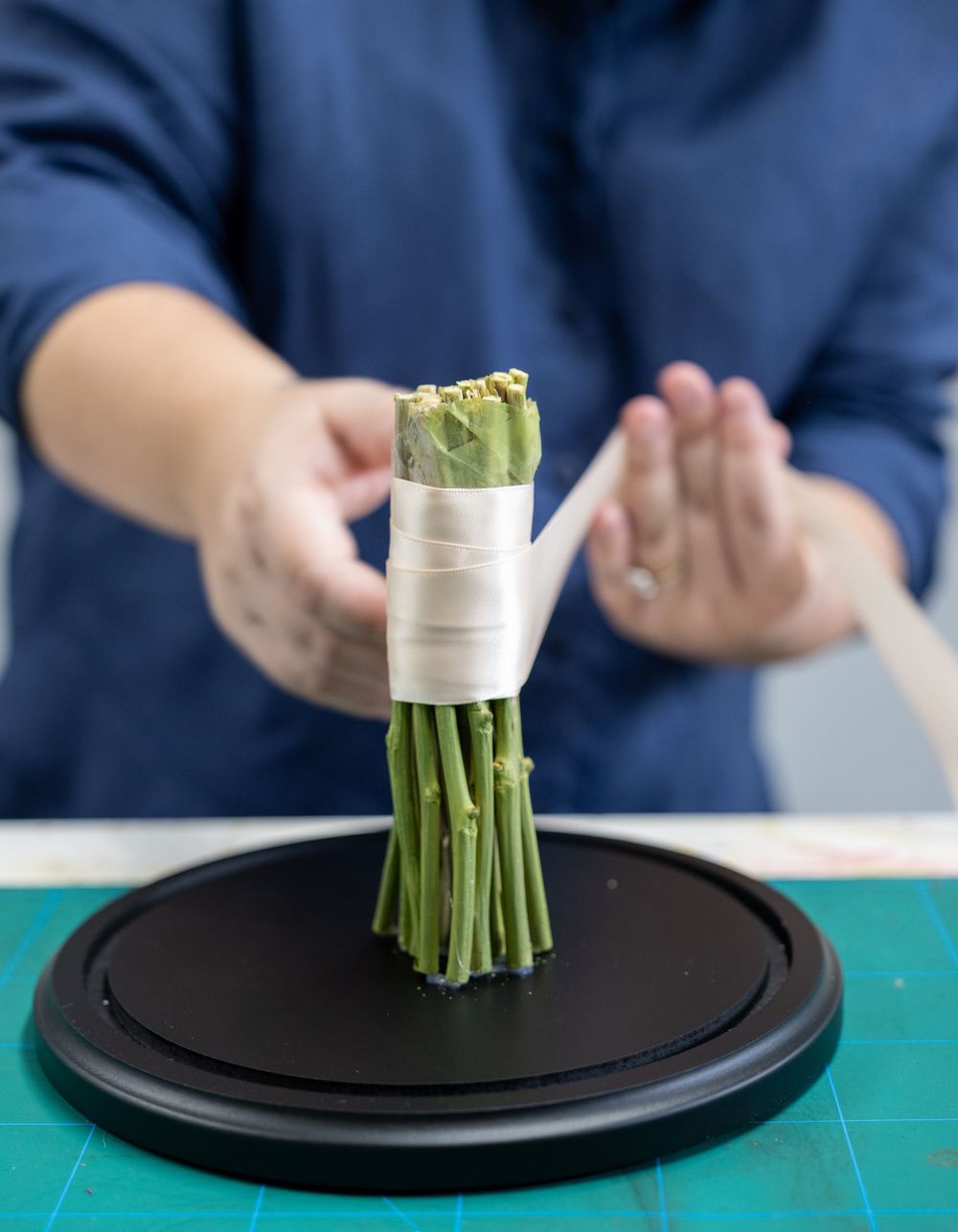 A hand places a bundle of asparagus wrapped in white paper onto a black serving plate.