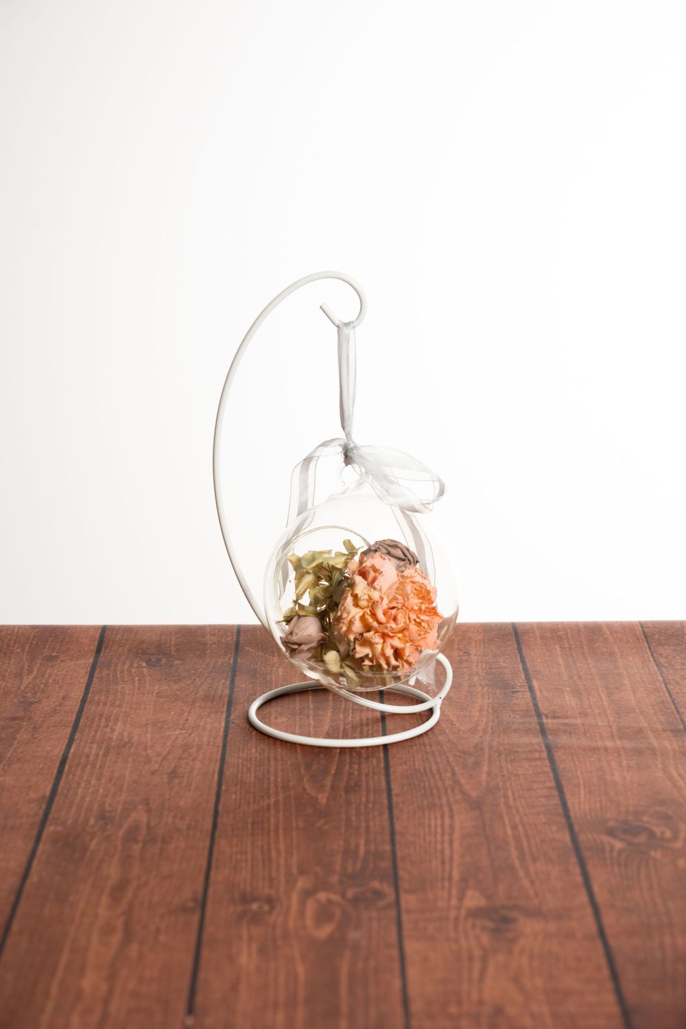 Glass terrarium with dried flowers and plants arranged in sequence showing progressive assembly on wooden table surface.