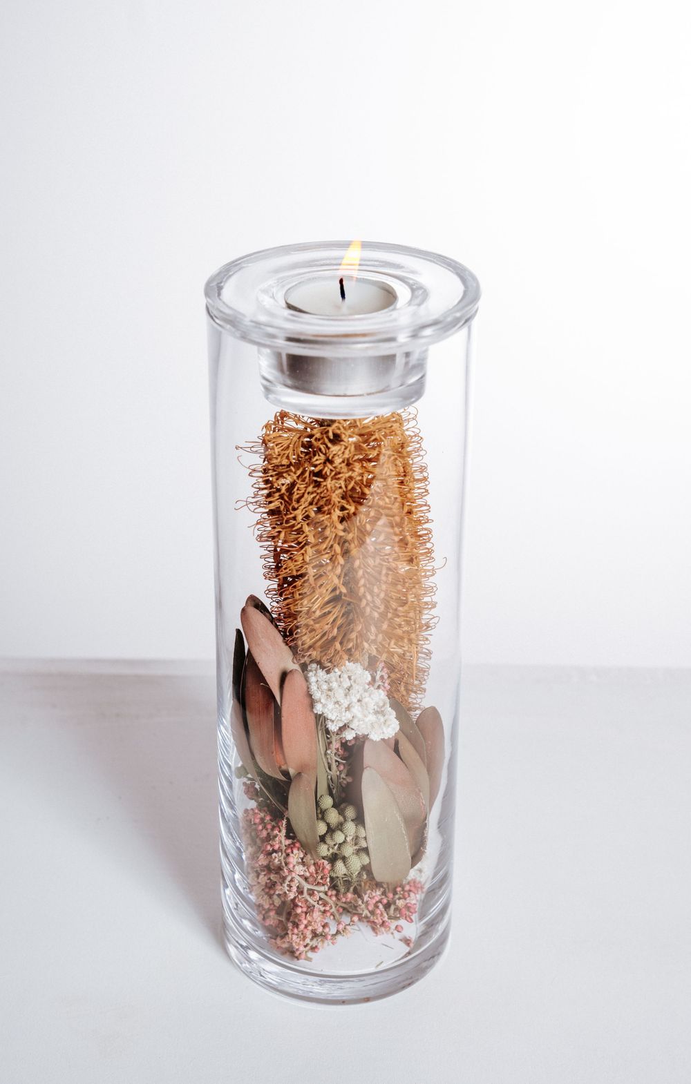 A series of glass jars containing preserved pink and white dried flowers with delicate foliage against a white background.