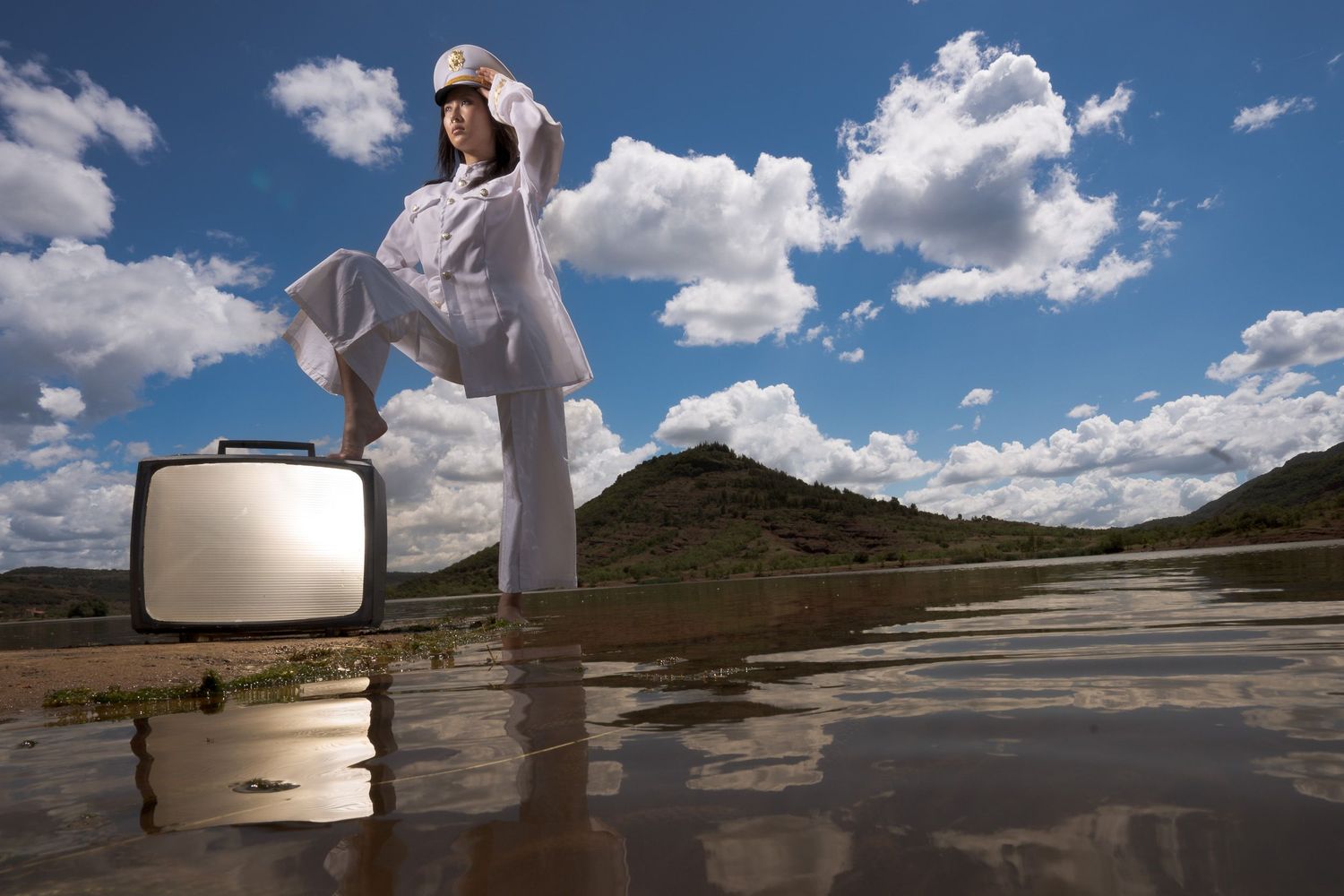 Figure in white standing on reflective surface against dramatic cloudy sky.