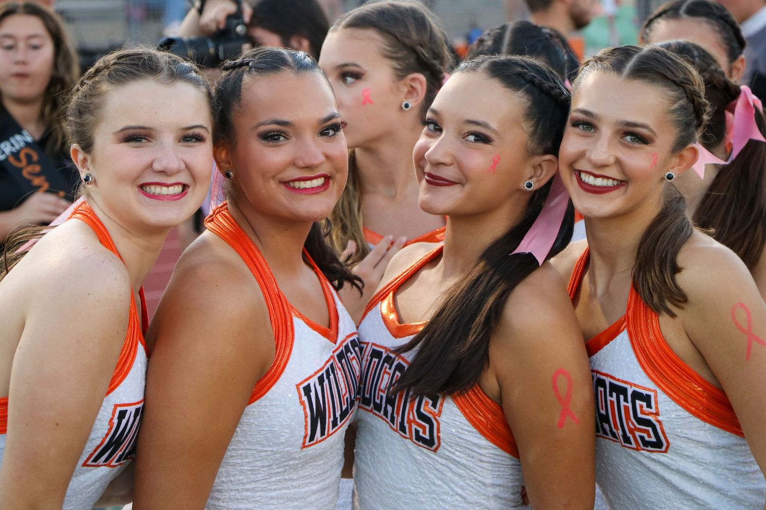 Group of cheerleaders in orange and white uniforms posing together at a sporting event.