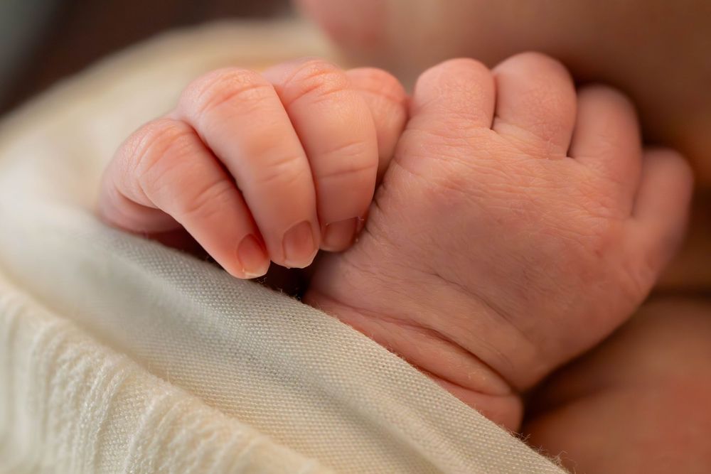 Close up of tiny baby feet resting on soft white fabric showing delicate toes and skin texture.