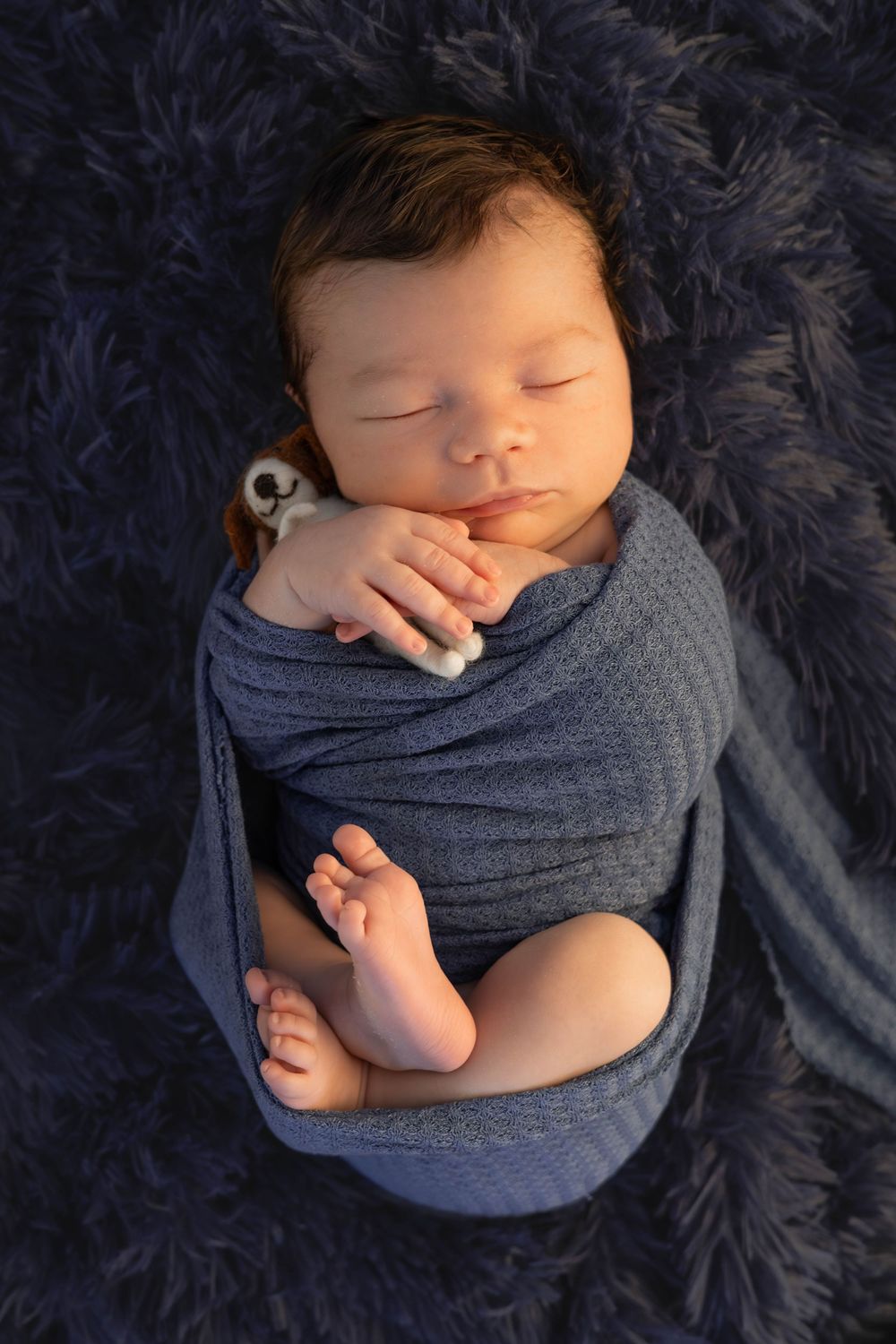 A sleeping newborn baby swaddled in soft gray fabric against a dark textured background.