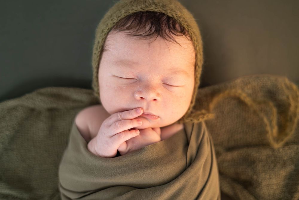 A series of close-up photos showing a sleeping baby's face, hands, and feet against a brown blanket background.