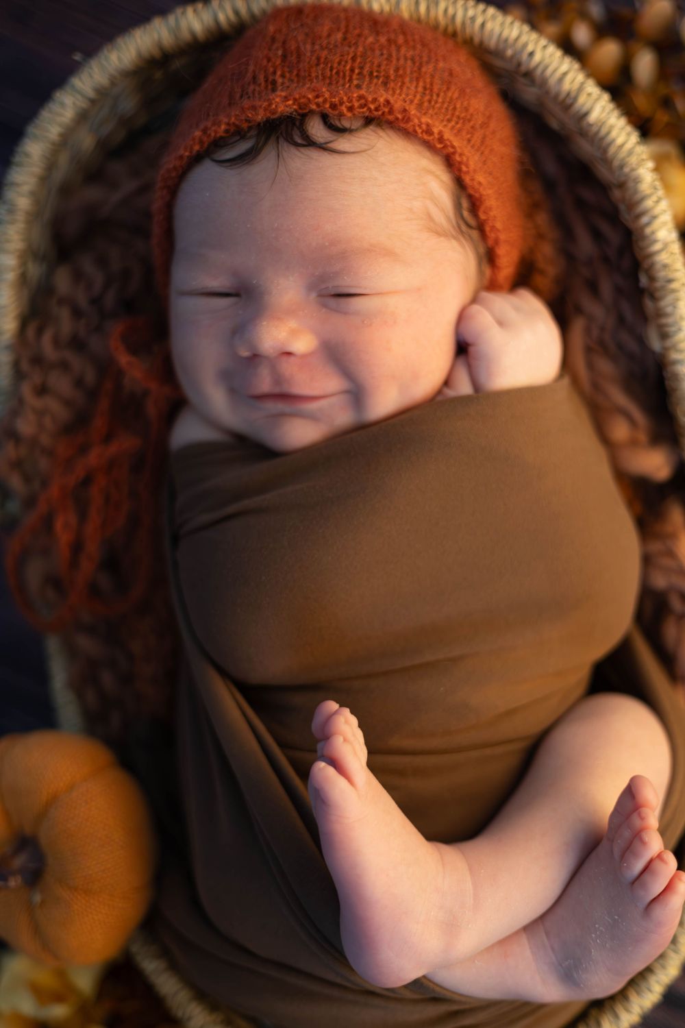A sleeping newborn baby swaddled in brown fabric rests peacefully in a cozy basket.