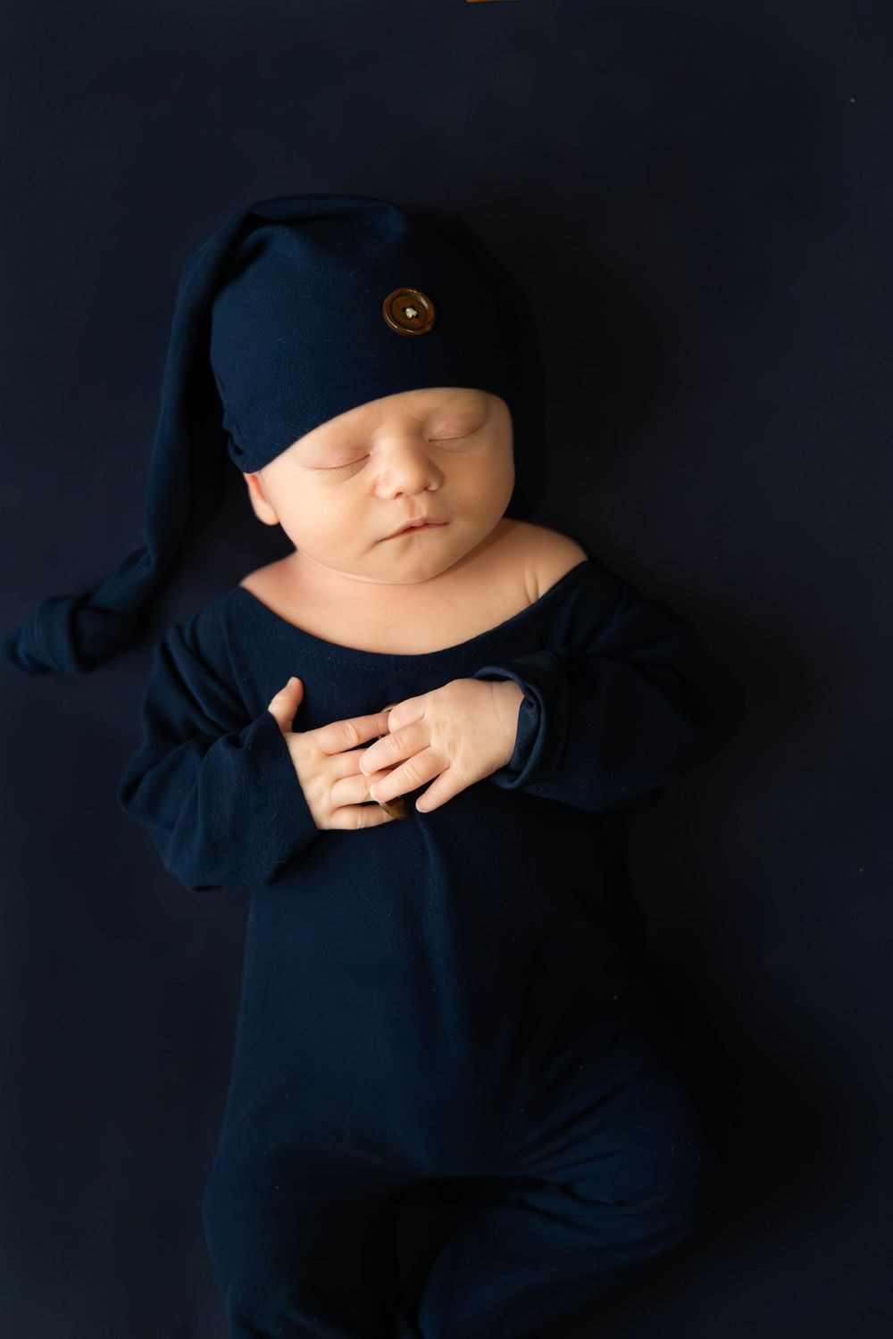 A sleeping baby wearing a navy blue outfit lies peacefully against a dark background in a series of artistic portraits.