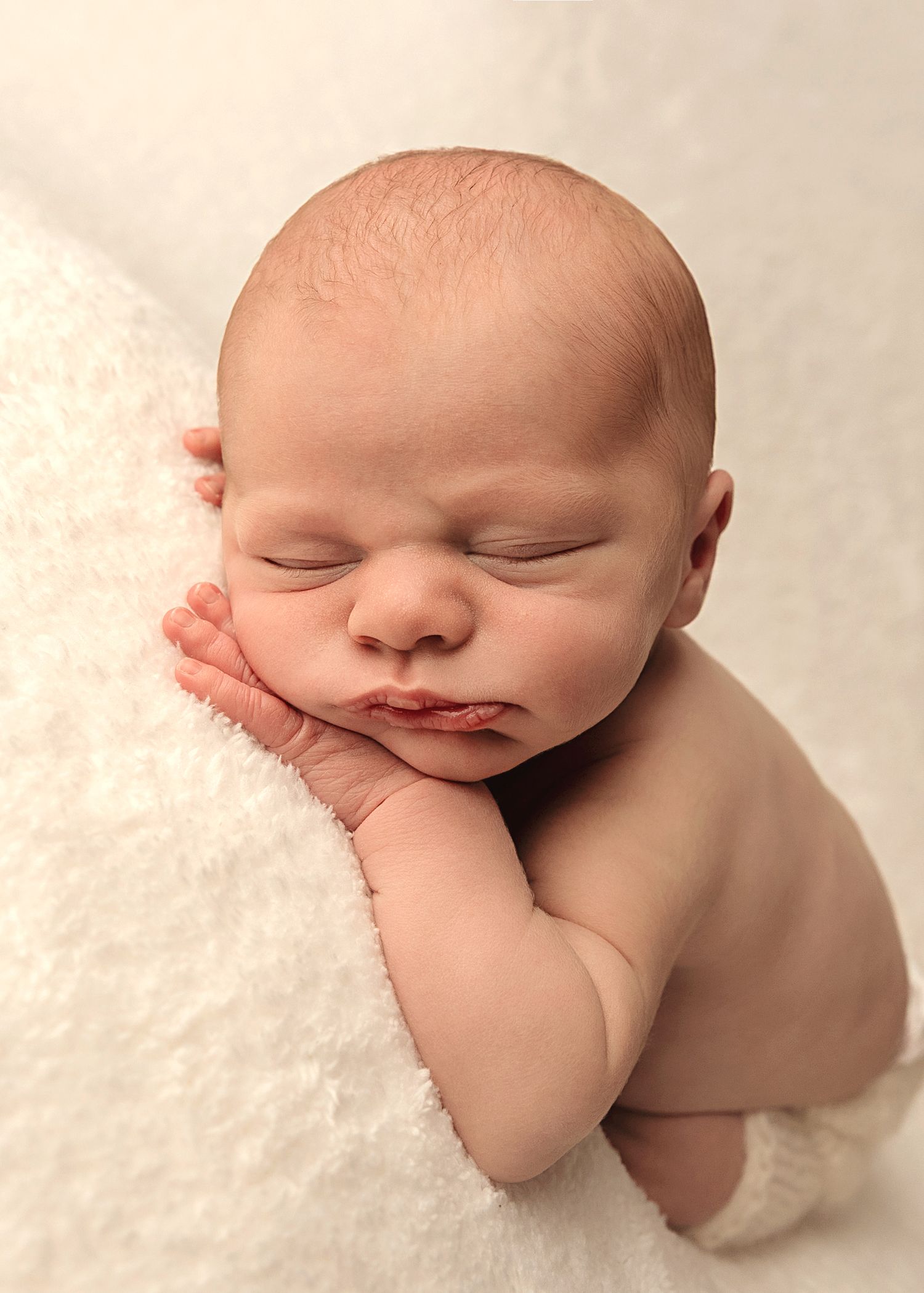 Picture of Baby boy on a fluffy white background with his head nestled on his hand