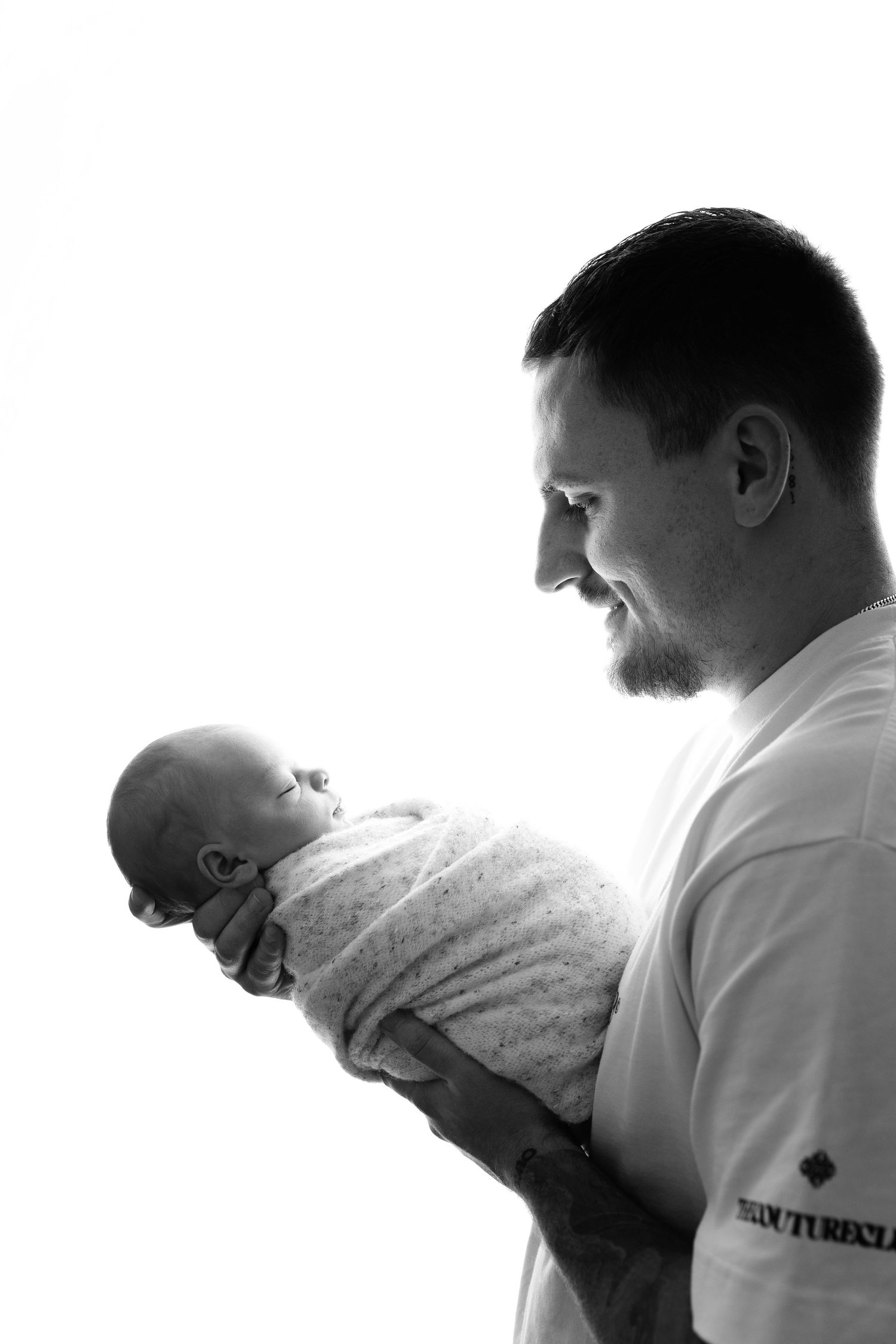 Black & White image of Dad holding his newborn baby boy and smiling taken in Shelly Loxton Photography's studio in Coventry