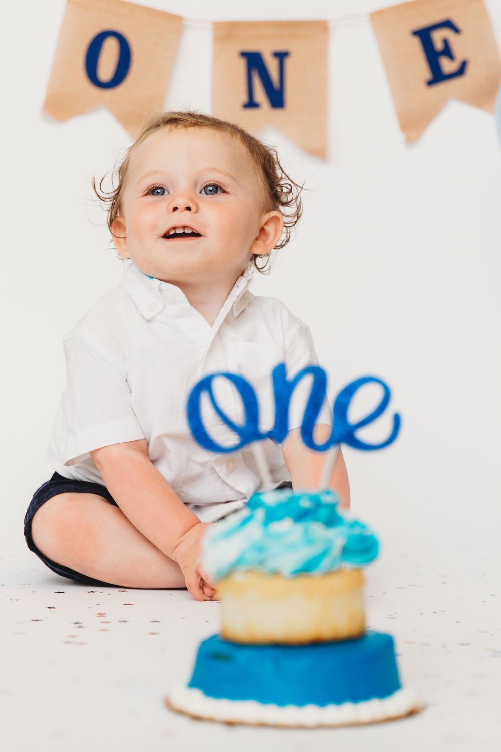 First birthday celebration with blue and white cake and 'ONE' banner decoration in peach tones.