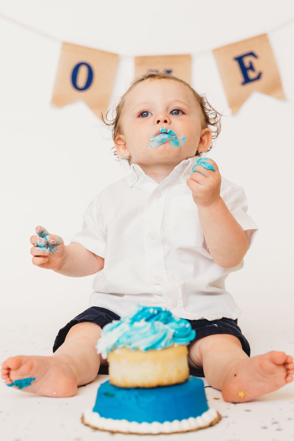 Baby with blue frosting on face enjoying first birthday cake.