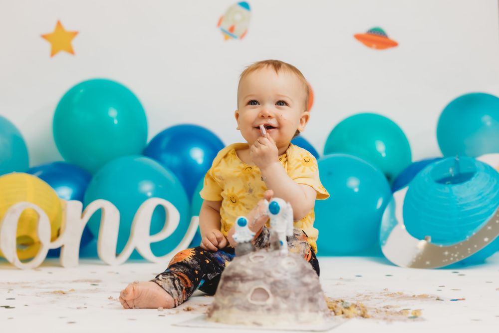 Happy baby in yellow shirt playing during space-themed first birthday photoshoot.