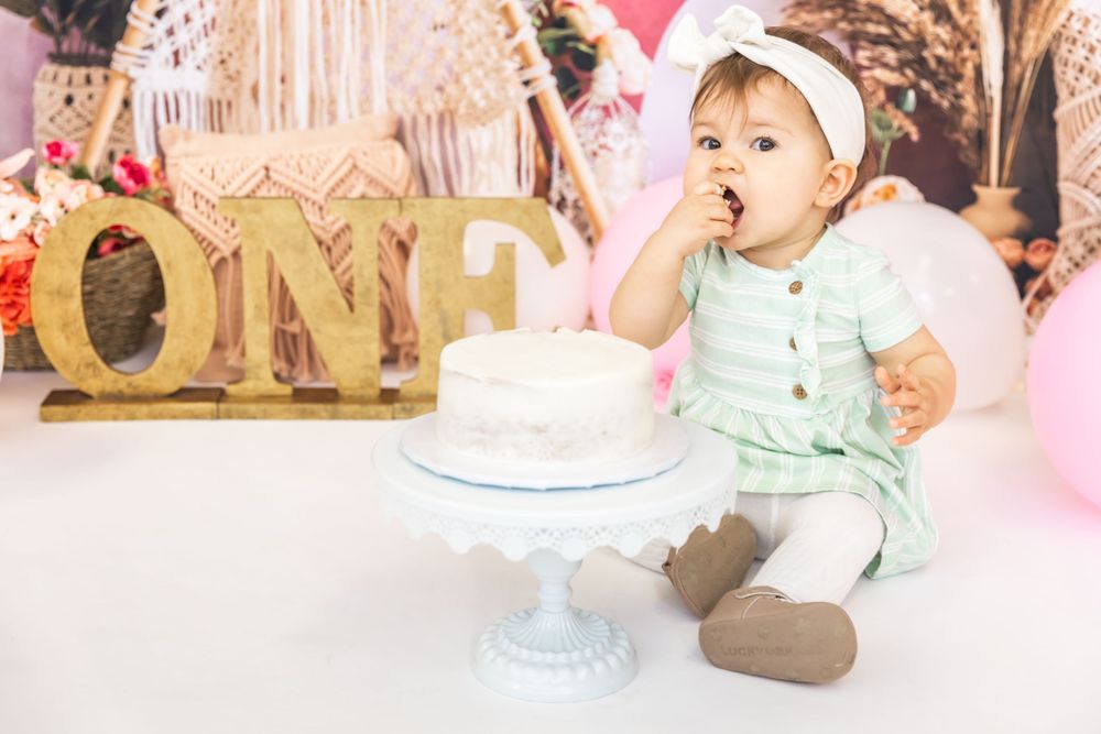 First birthday setup with gold 'ONE' letters and white cake on pedestal.