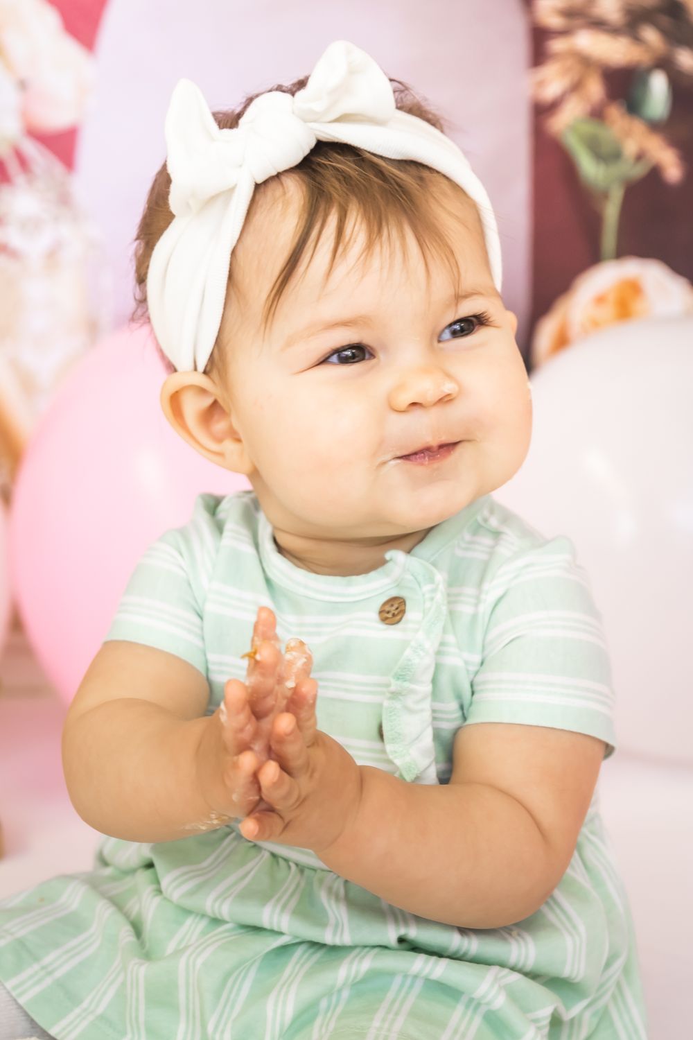 Baby in mint striped dress with white bow headband during birthday photoshoot.