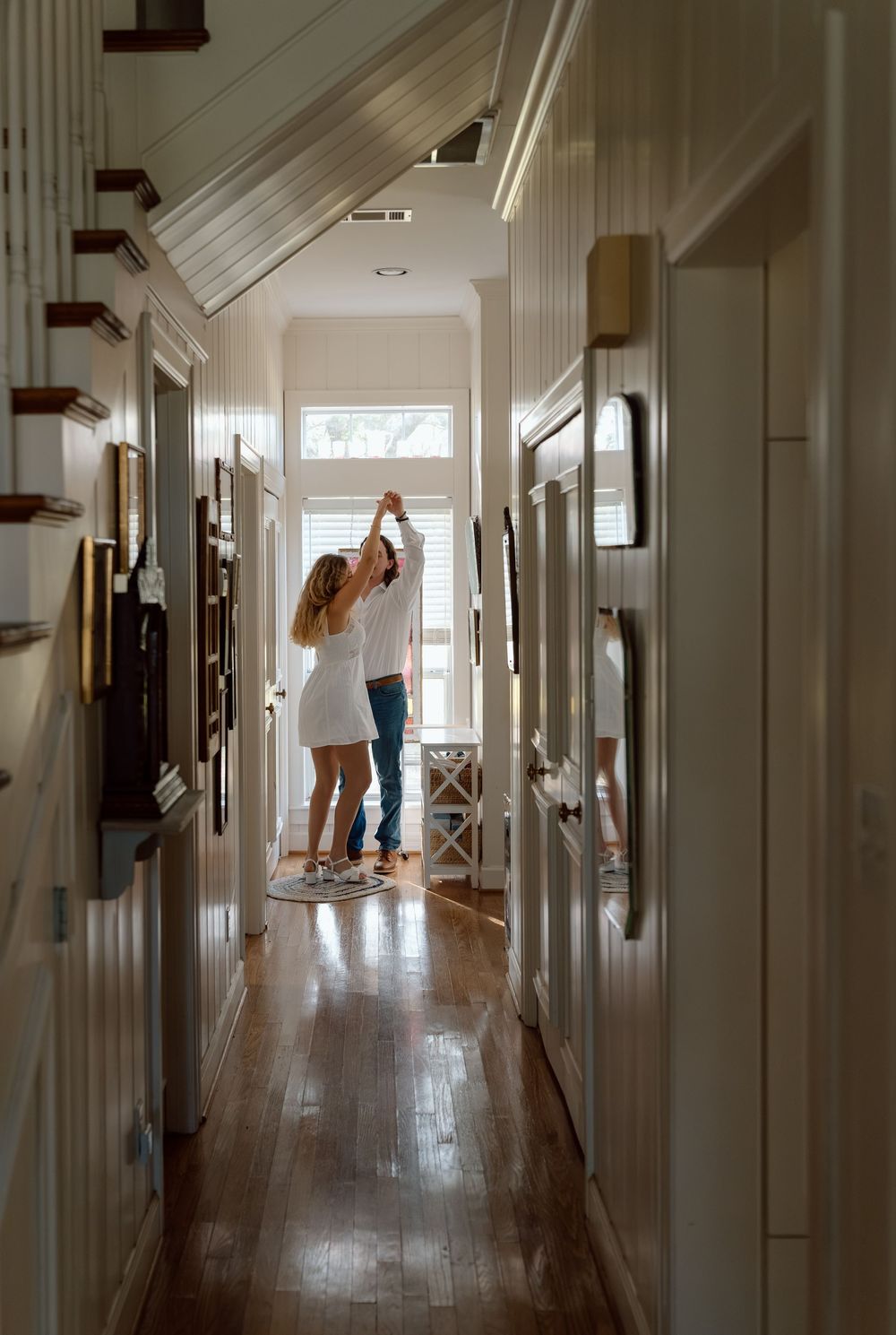 Couple dancing together in a bright white hallway with hardwood floors.