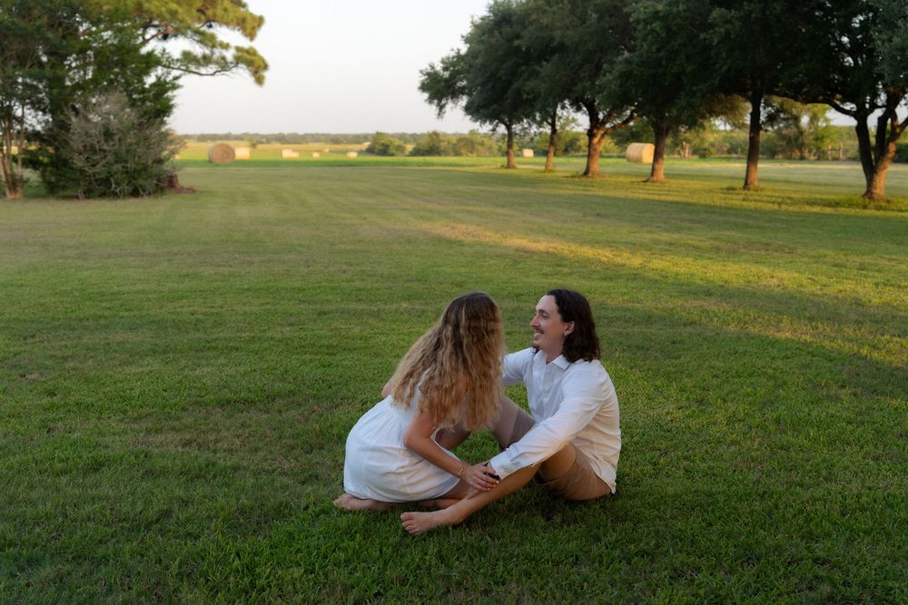 Couple sitting together on lush green grass in a park, facing each other and holding hands at sunset.