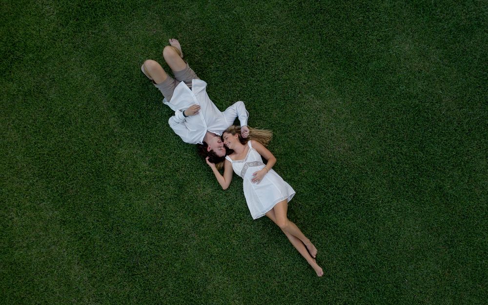 Aerial view of a couple in white outfits lying on lush green grass, relaxing side by side outdoors.