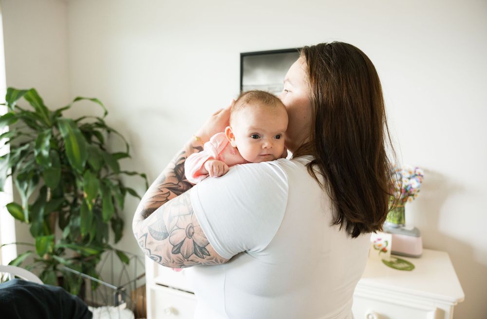 Adult in white shirt holding and comforting small baby near indoor plants.