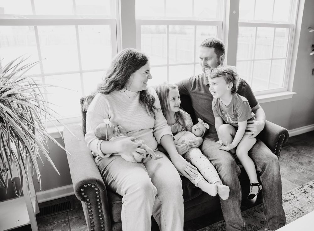 A family sits together on a couch by a window sharing a joyful moment in black and white photography.