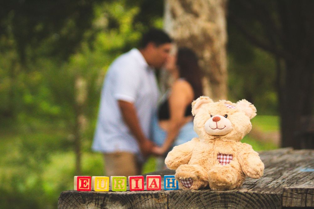 Teddy bear and alphabet blocks arranged in foreground with couple blurred in background.