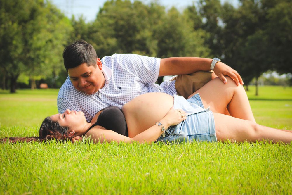 Couple laying on grass during outdoor maternity photoshoot session.