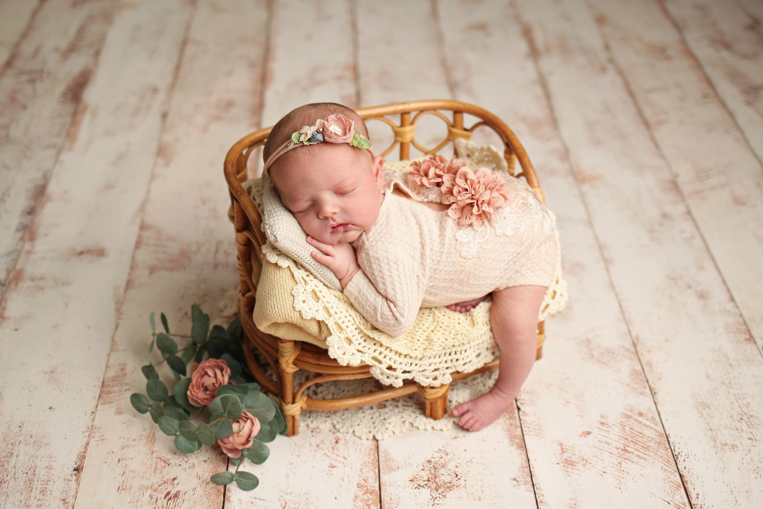 Peaceful newborn baby in cream lace wrap resting in wooden crib with pink roses.