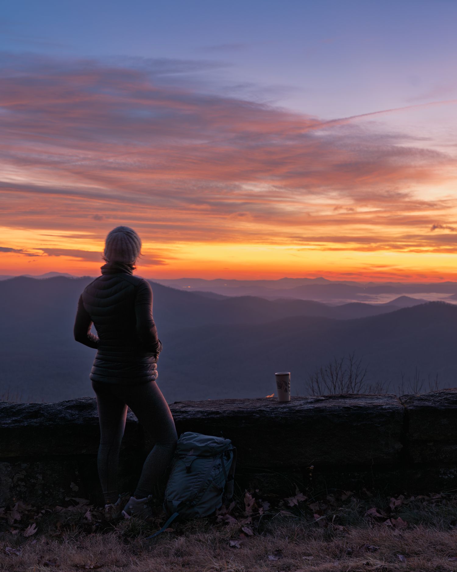 A seated hiker takes in the view of the Blue Ridge Mountains at dusk.