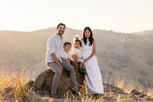 Family of four smiling on a rock at golden hour with rolling hills in the background.