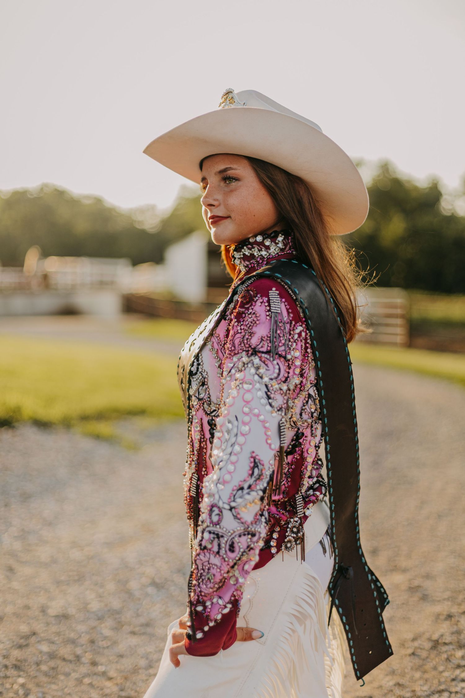A person in a white cowboy hat and floral print top poses in golden sunlight on a dirt path.