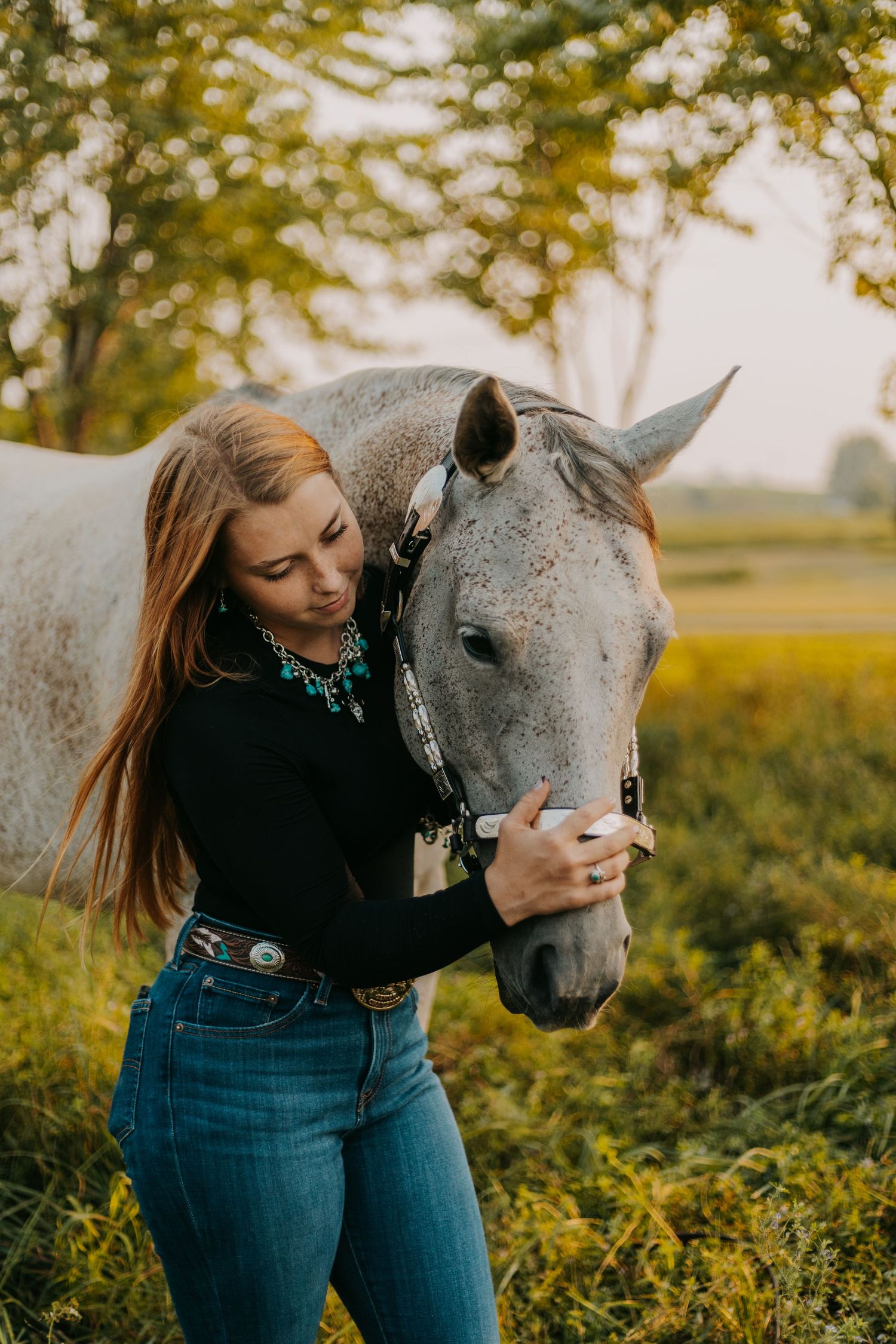 A dapple gray horse and rider share a tender moment in a sunlit field during golden hour.
