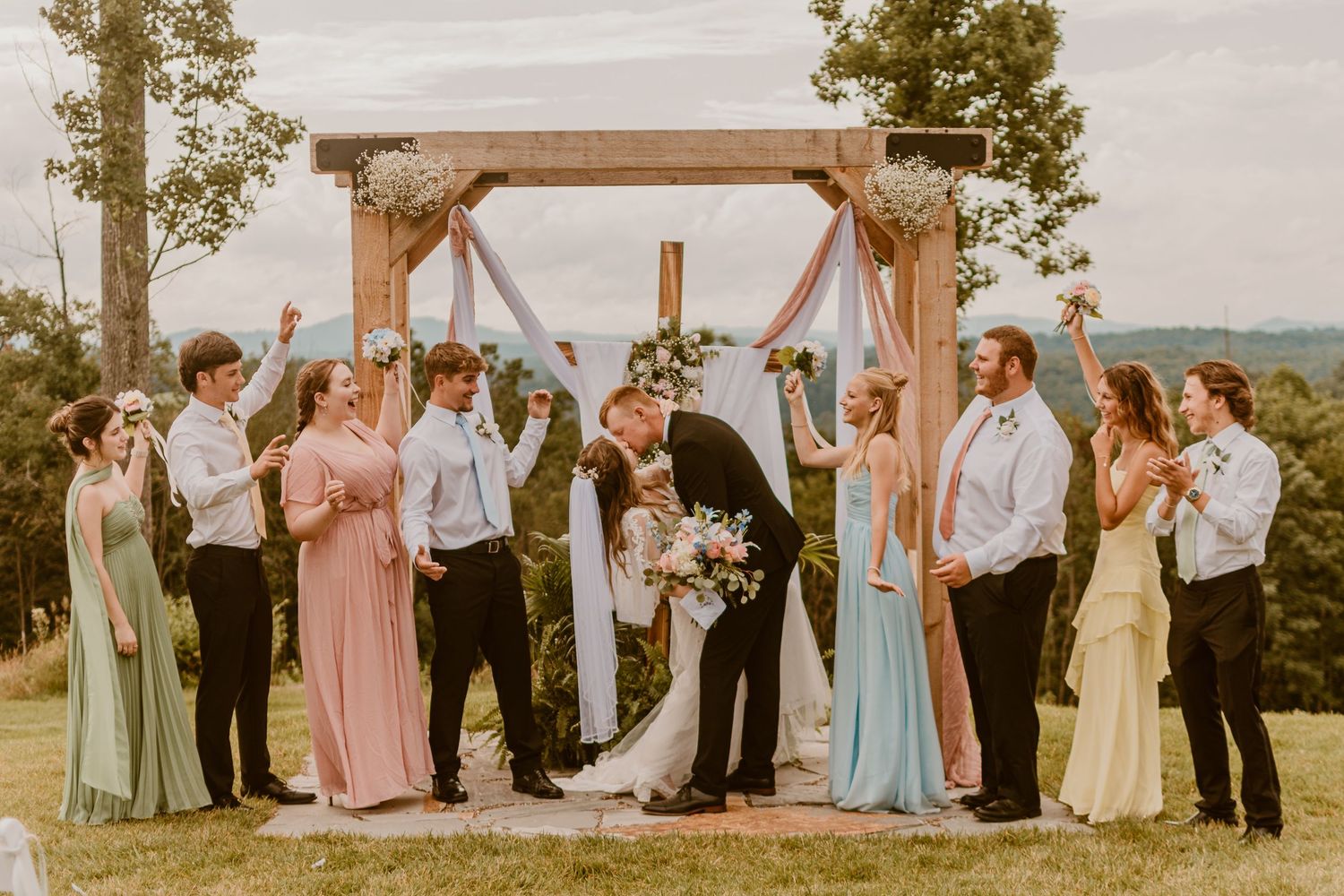 A romantic outdoor wedding ceremony setup with white chairs and lanterns along a tree-lined path.