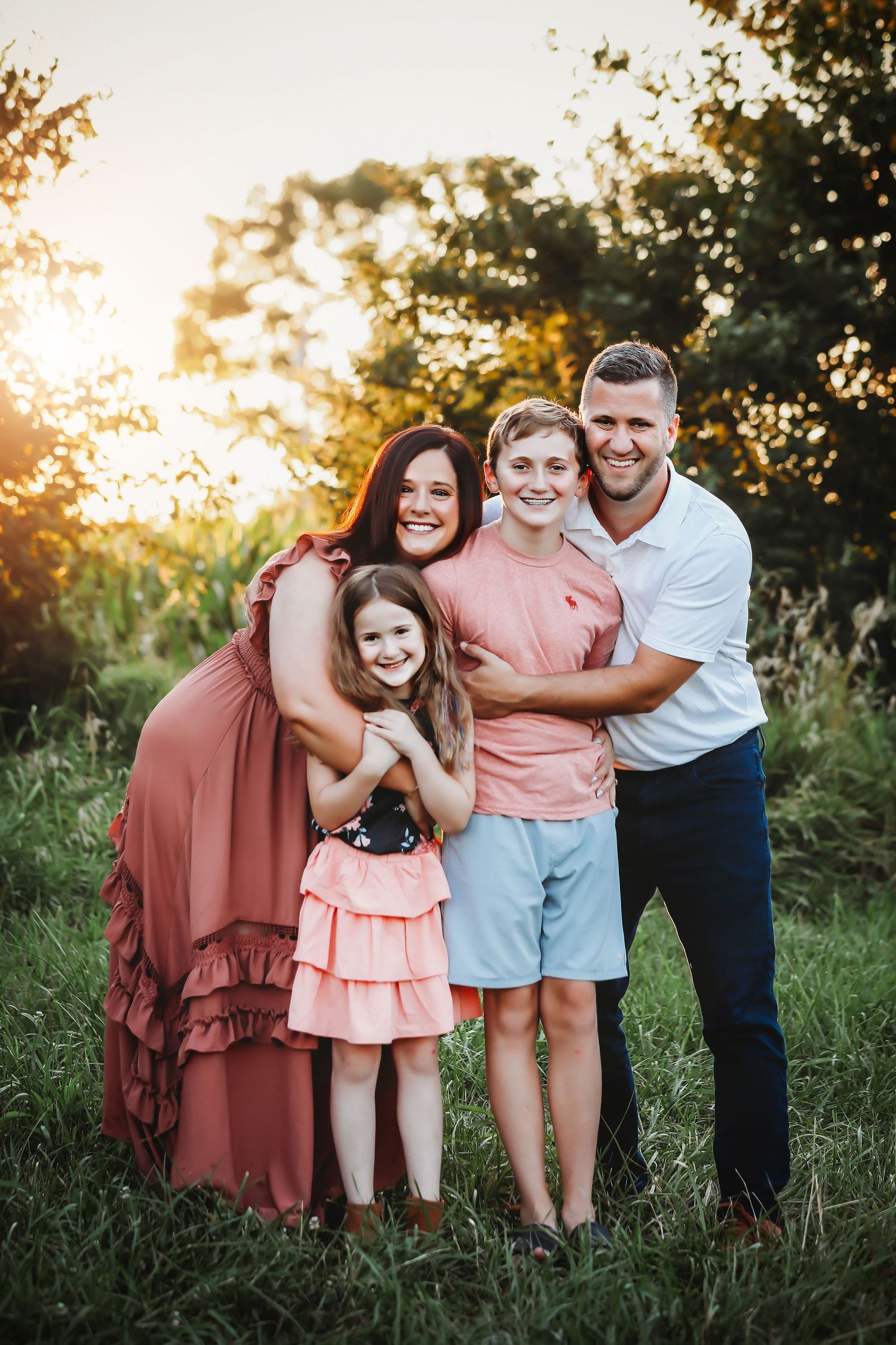 Family of four posing together outdoors during sunset in a field with tall grass.