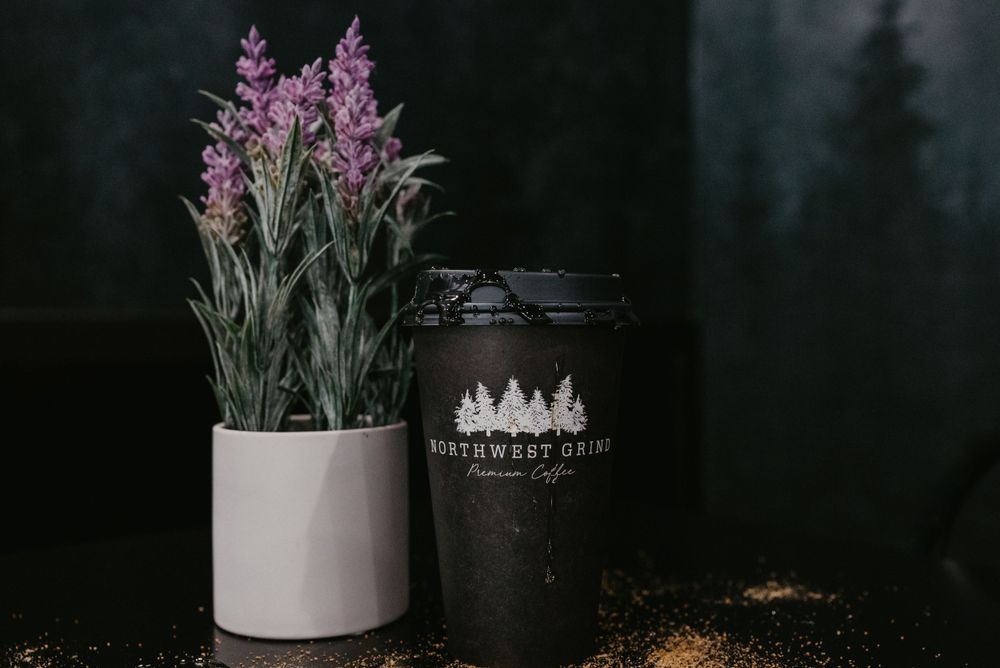 Purple flowers in white planter next to black branded tumbler cup.