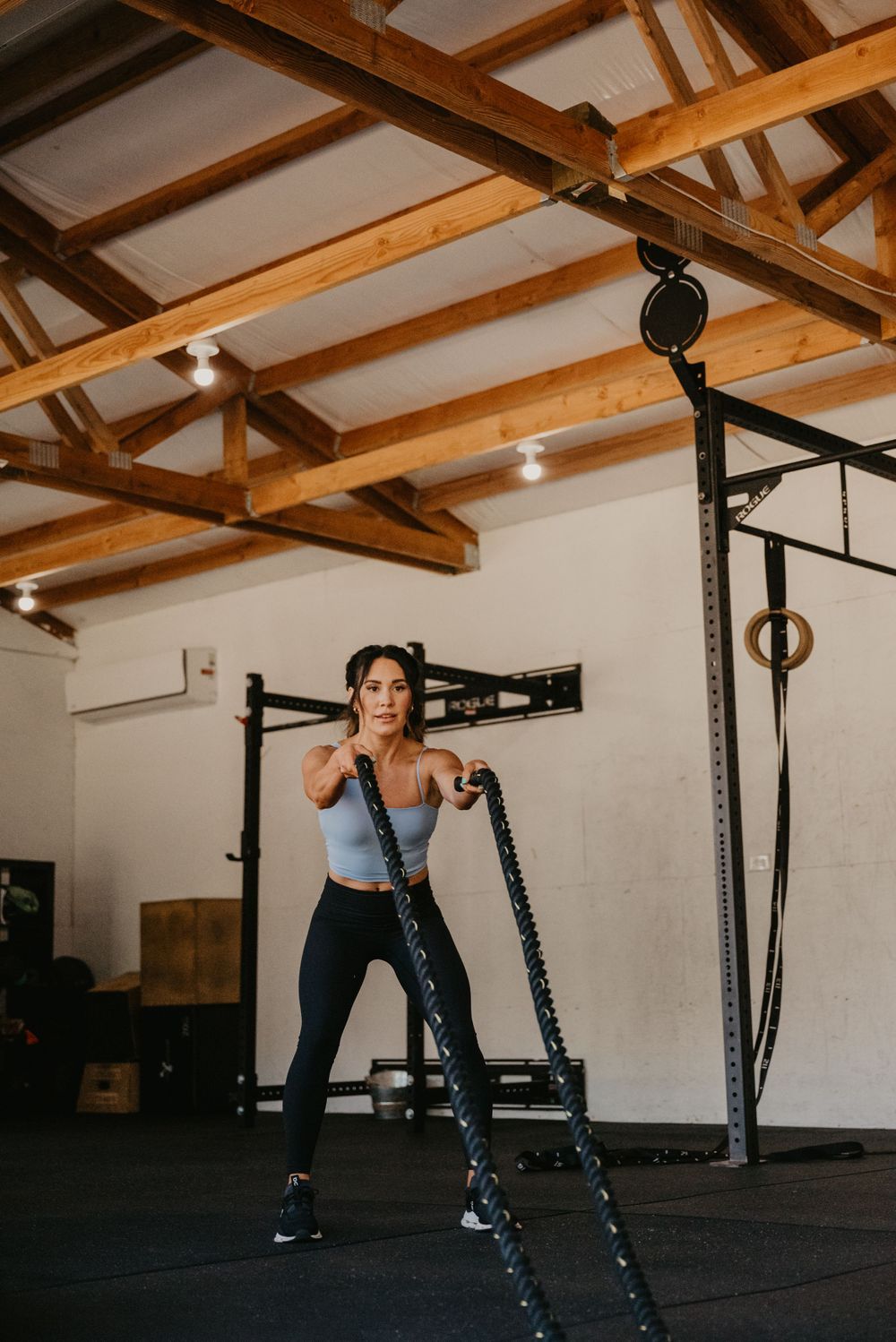 Athletic person performing battle rope exercise in a rustic gym with exposed wooden beams.